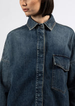 The Rosa Denim Over Shirt features an oversized fit, authentic denim material, and a medium wash. It also has a front patch pocket and concealed button fastening, along with a logo label on the back.